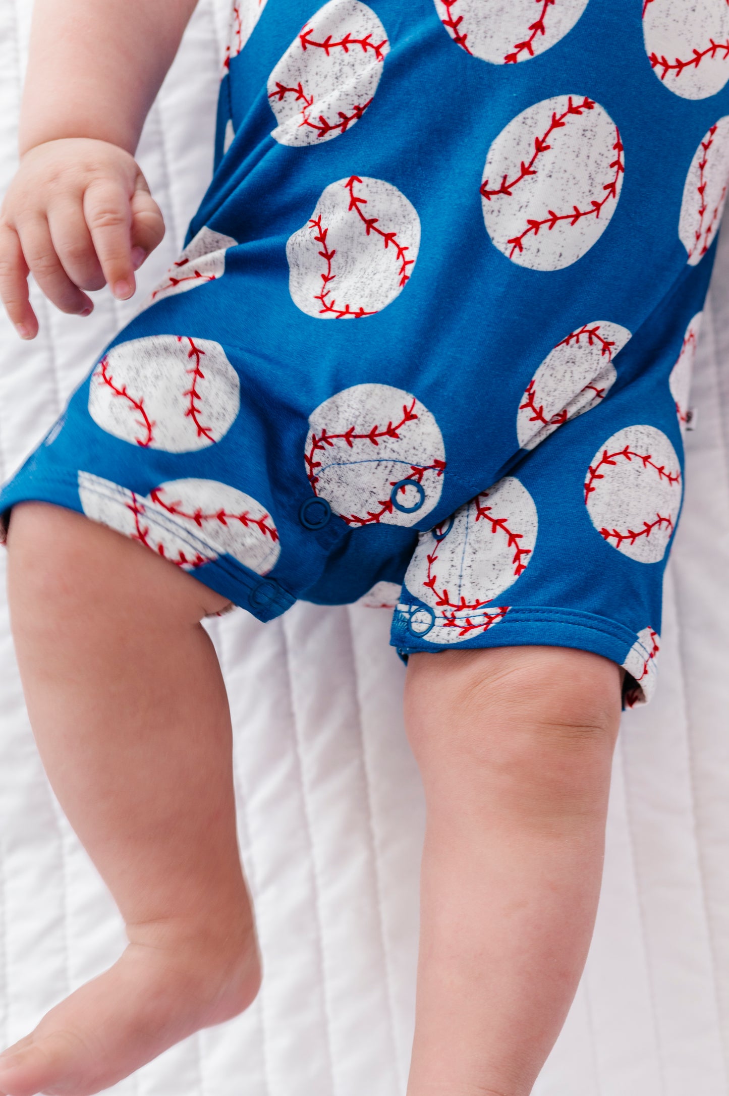 Baby wearing blue bamboo romper with baseball pattern on a white background