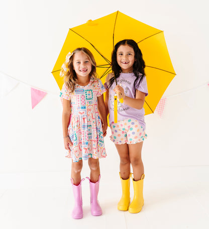 Two children holding a yellow umbrella on a white background