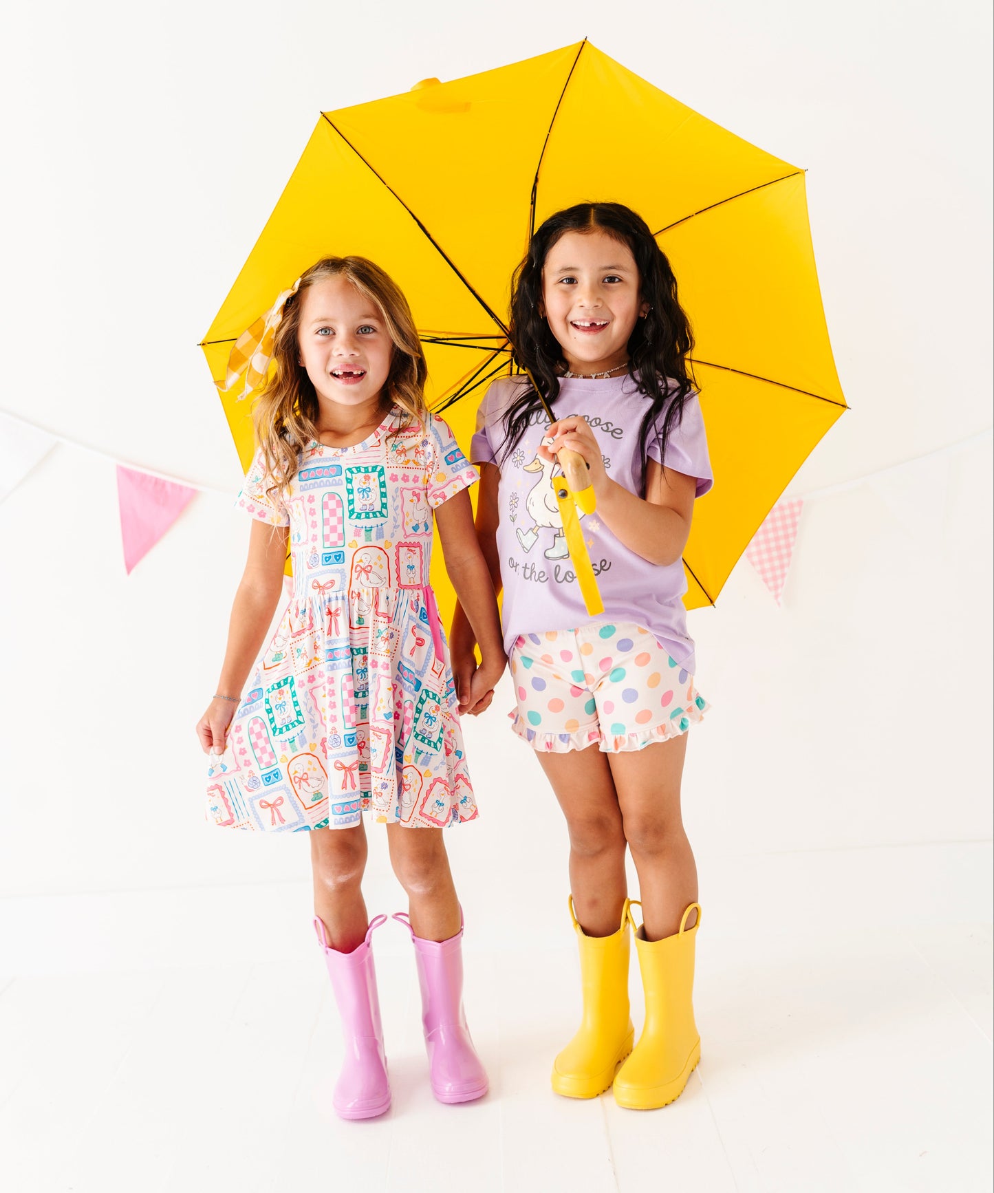 Two children holding a yellow umbrella on a white background