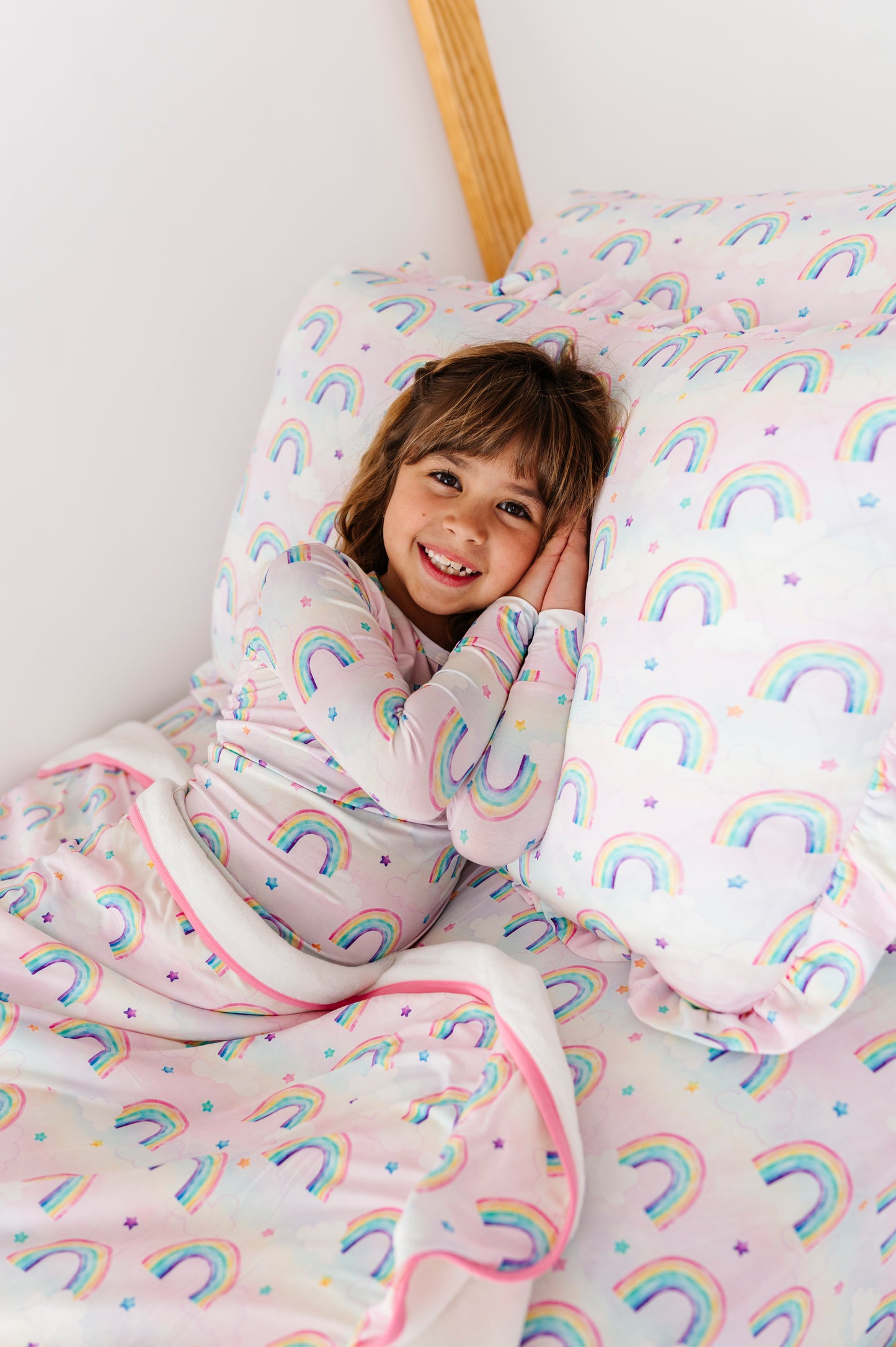 Child in a rainbow-patterned room, smiling and leaning against a pillow with rainbows.