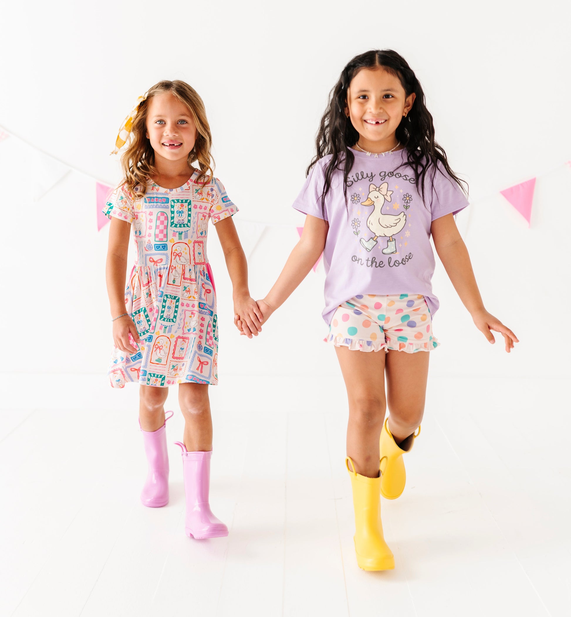 Two young girls wearing colorful outfits with rain boots on a white background