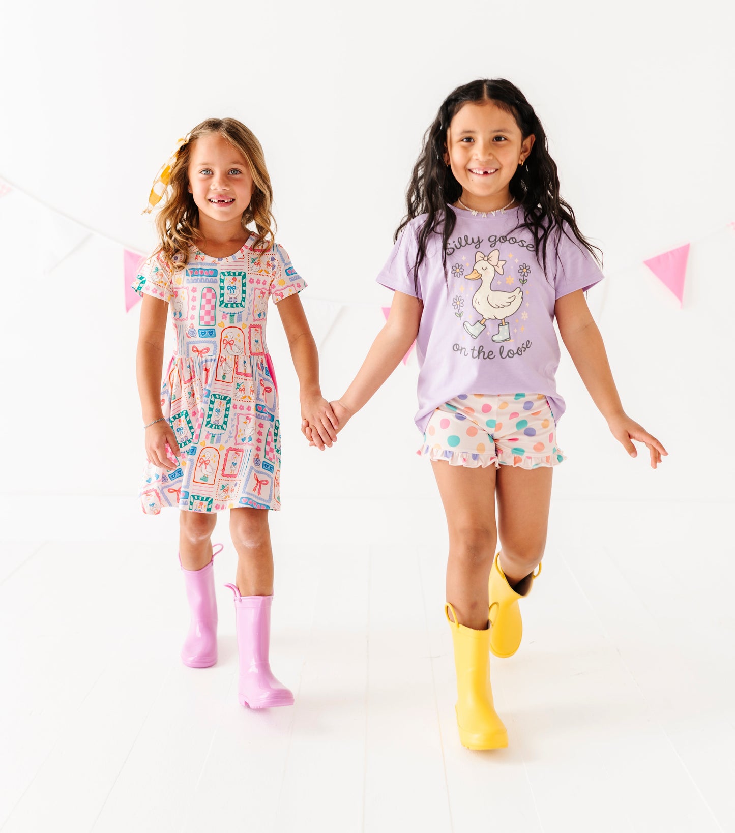 Two young girls wearing colorful bamboo outfits with rain boots on a white background