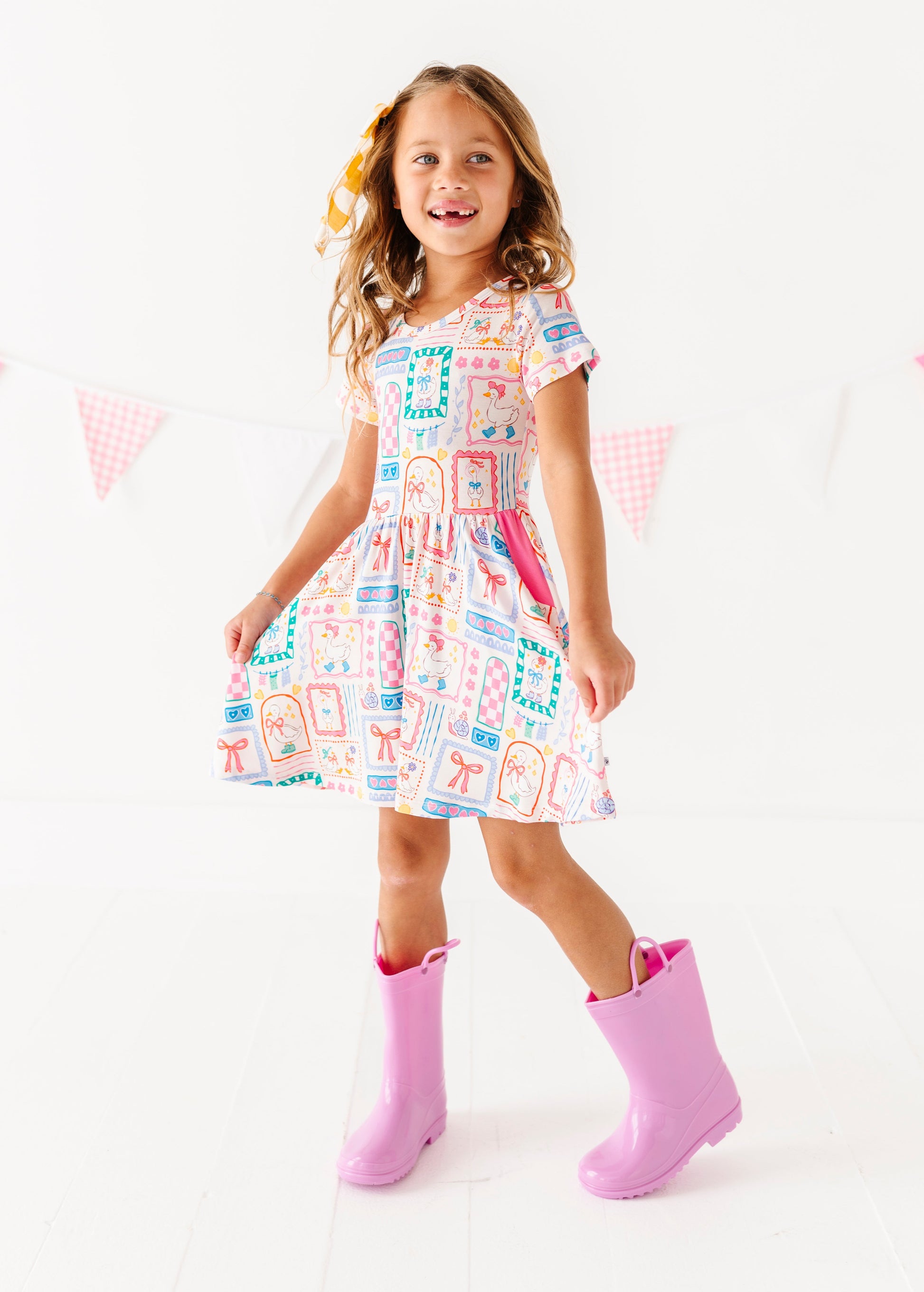 Young girl wearing a colorful bamboo dress and pink rain boots on a white background