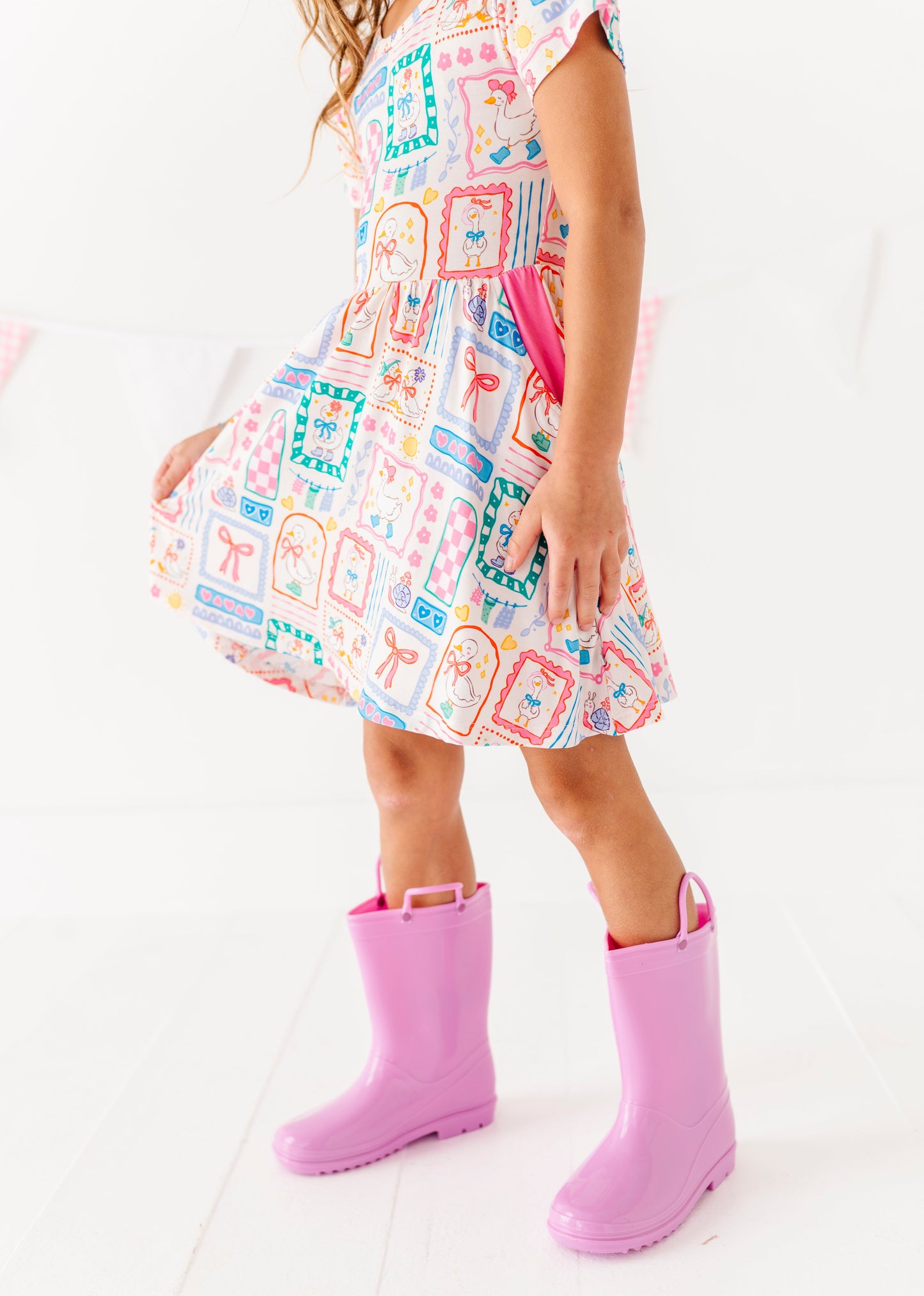 Child wearing a colorful bamboo dress with geometric patterns and pink rain boots on a white background