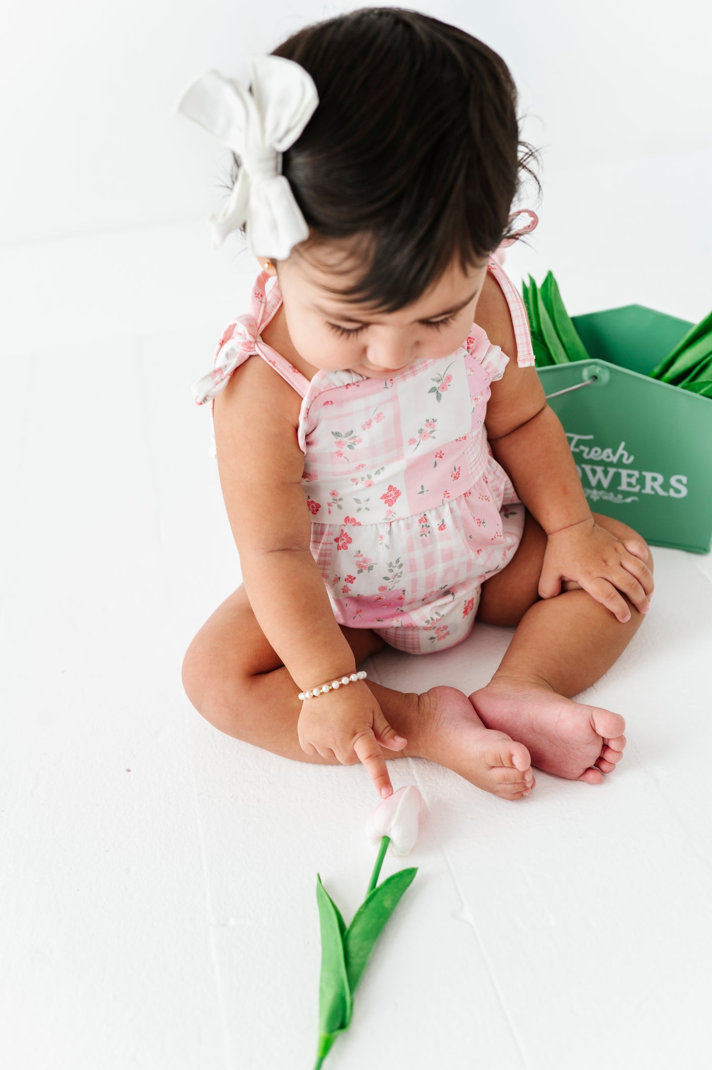 Baby in a floral bamboo outfit holding a tulip on a white background