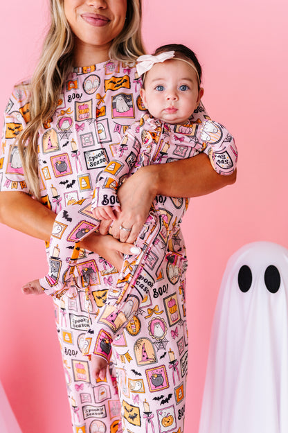 A woman holding a baby wearing a matching Halloween-themed pajama set. The pajamas feature a pink background with a collage of spooky illustrations like ghosts, bats, pumpkins, and the words 'good night' and '800$'.