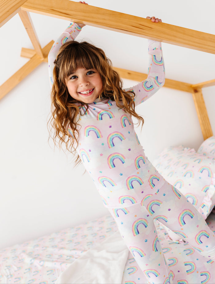 Child wearing rainbow-patterned bamboo pajamas in a bedroom setting