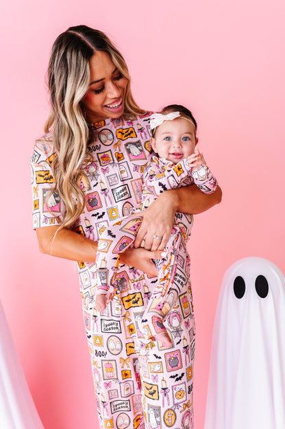 A woman and a baby wearing matching pajamas with a colorful vintage mailer envelope print, posed against a solid pink background with a white ghost prop.