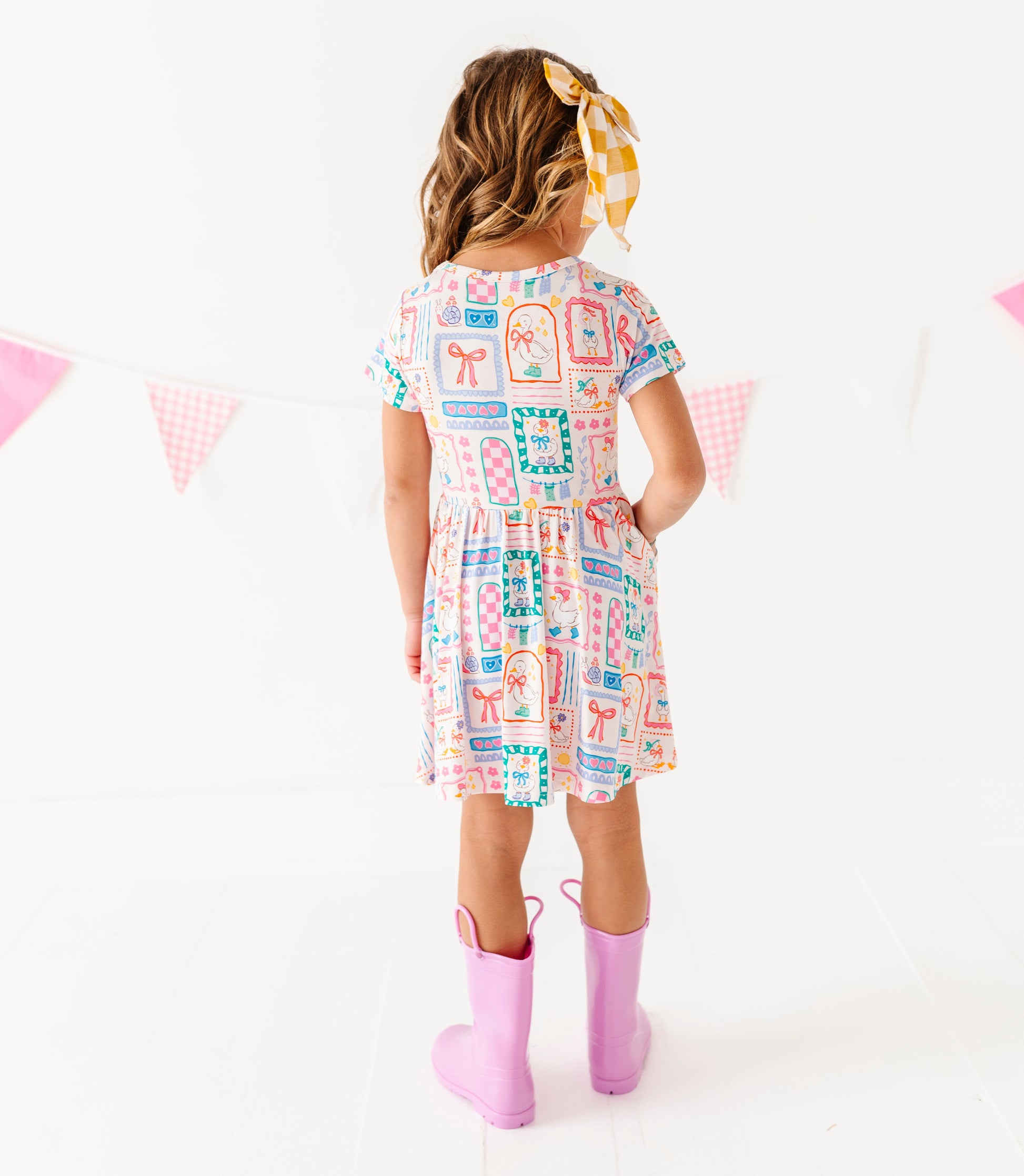 Child wearing a colorful dress with a pattern of various shapes and colors, standing against a white background.