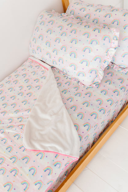 Children's bed with rainbow-patterned bamboo bedding on a white floor.