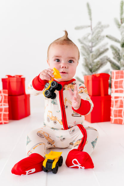 A baby playing with construction trucks while wearing a Christmas construction-themed convertible romper. It's a super soft bamboo zip romper 