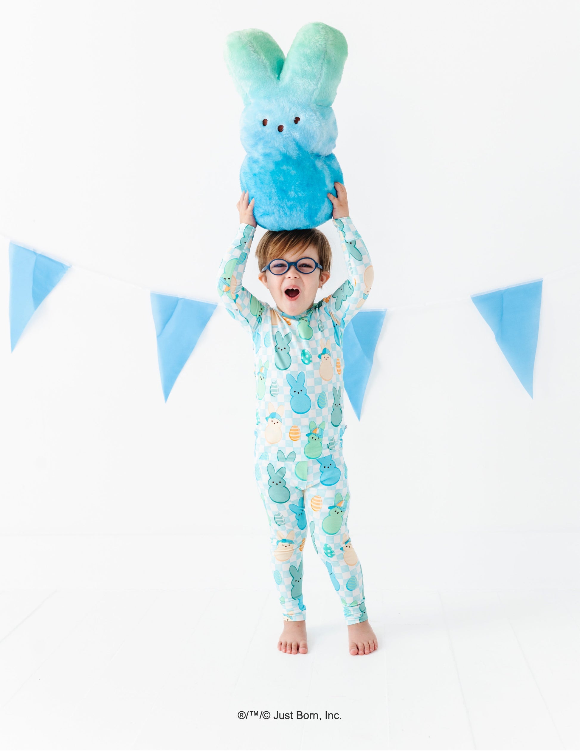 Child wearing a pajama set with a blue and green plush PEEPS® toy above their head against a white background with blue triangular flags.