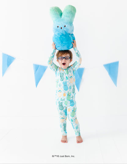 Child wearing a pajama set with a blue and green plush PEEPS® toy above their head against a white background with blue triangular flags.