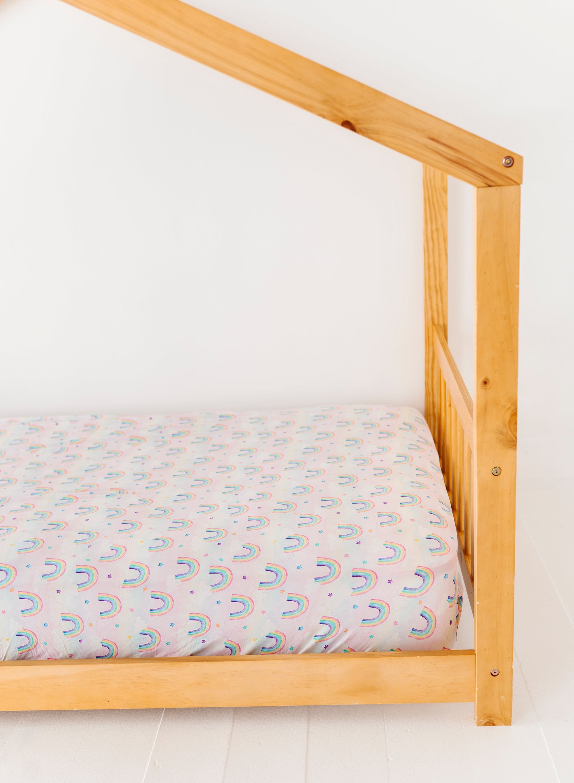 Wooden bed frame with a  bamboo twin sheet featuring colorful watercolor rainbows on a white background