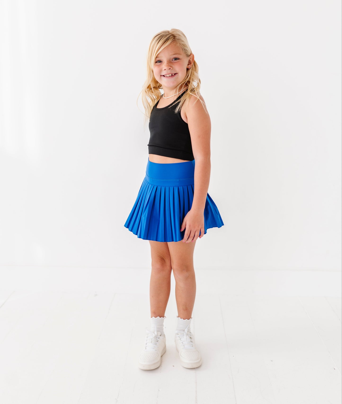 Young girl wearing a black top and blue active skort on a white background