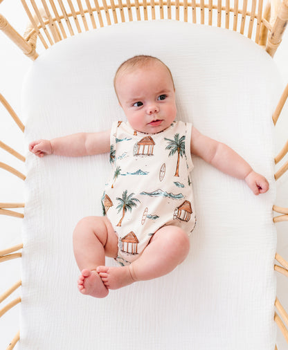 Baby lying in a crib wearing a onesie with a beach-themed design.