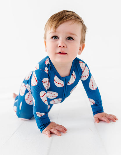 Baby wearing a blue bamboo romper with a baseball pattern, crawling on a white surface.