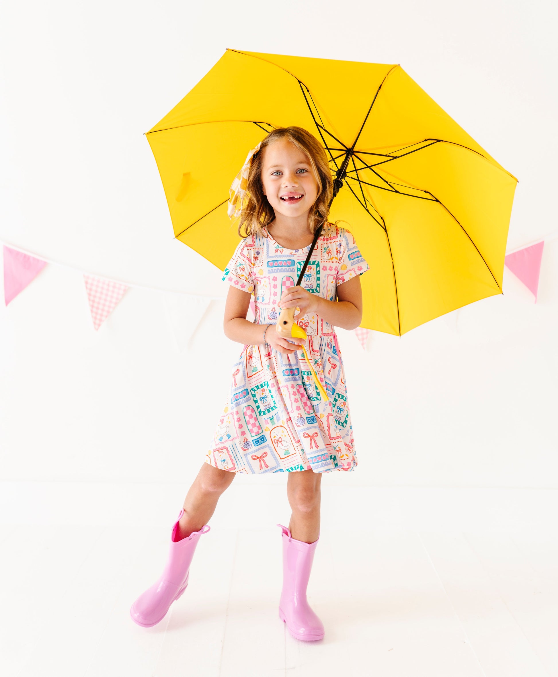 Child holding a yellow umbrella on a white background wearing a bamboo dress and rain boots