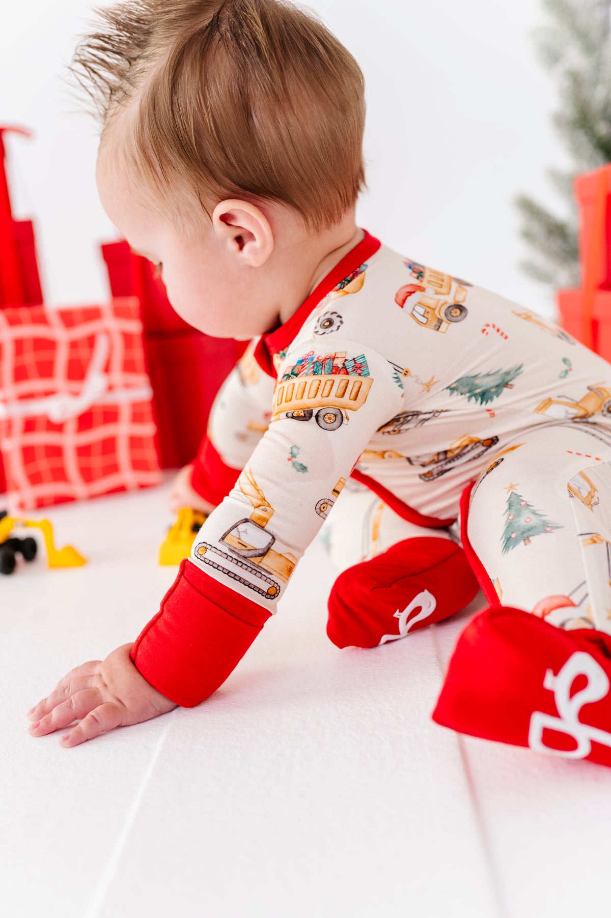 A baby boy playing with construction trucks like dump trucks and excavators. He's wearing a matching Christmas construction truck themed bamboo zip romper 