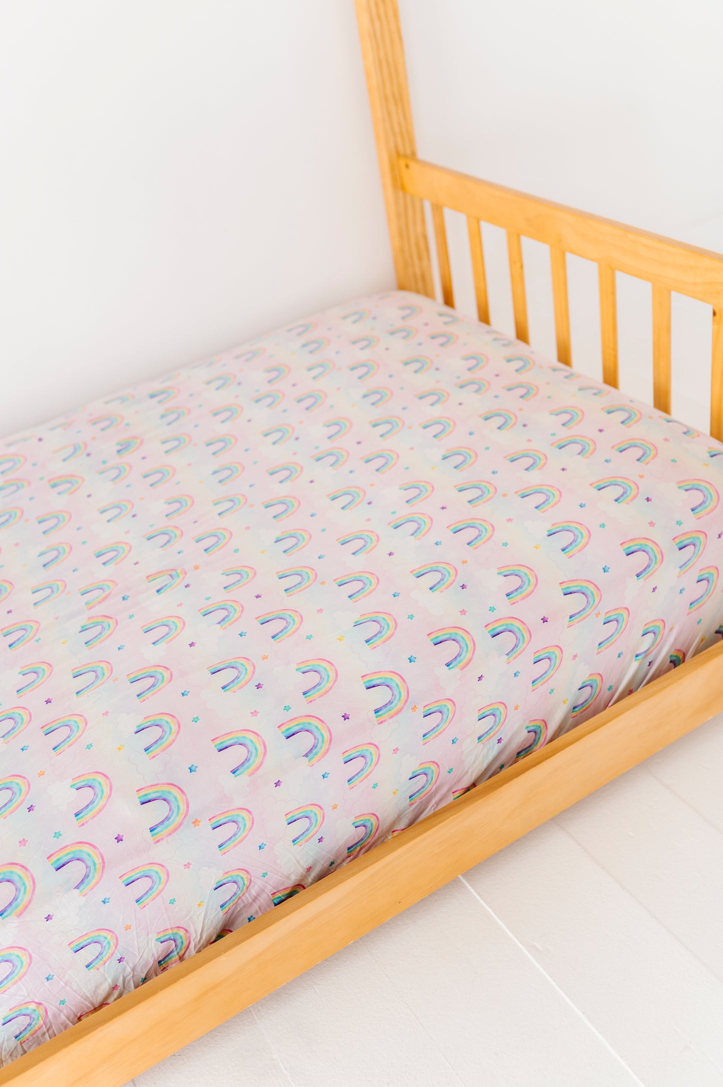 Twin-size bed with a watercolor rainbow-patterned bamboo mattress cover on a white floor.