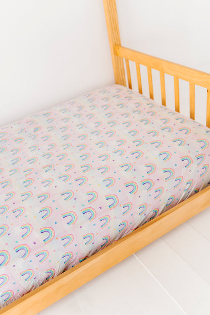 Twin-size bed with a watercolor rainbow-patterned bamboo mattress cover on a white floor.