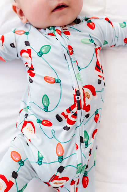 A close-up detail shot of a little boy wearing a blue bamboo convertible romper featuring Santa Claus hanging from multi-colored Christmas lights