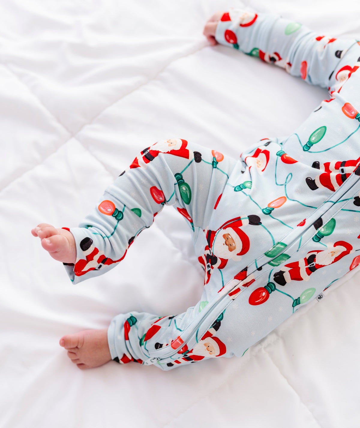 A close-up detail shot of a little boy wearing a blue bamboo zip romper featuring Santa Claus hanging from multi-colored Christmas lights