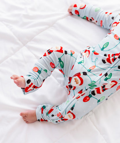A close-up detail shot of a little boy wearing a blue bamboo zip romper featuring Santa Claus hanging from multi-colored Christmas lights