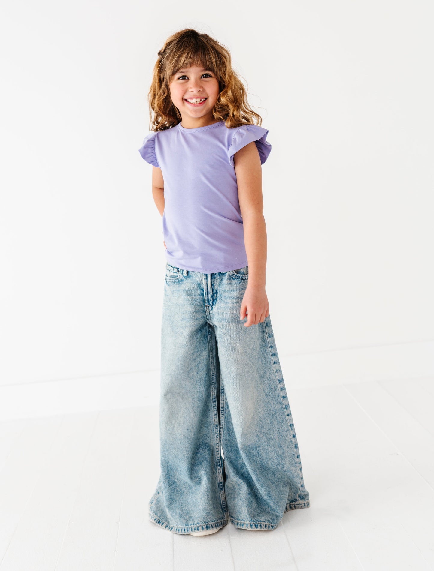 Young girl wearing a purple bamboo/cotton shirt and wide-leg jeans on a white background