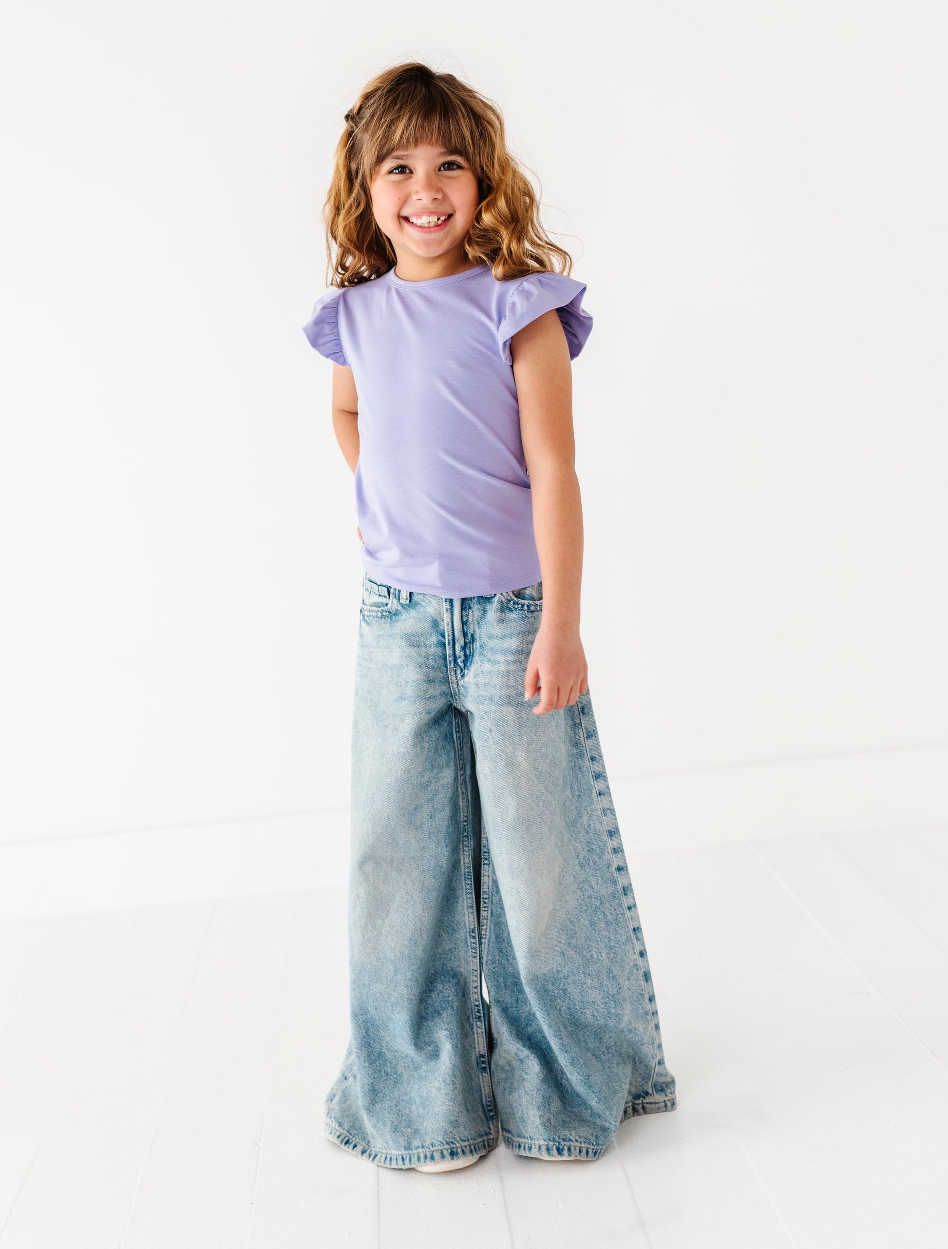 Young girl wearing a purple bamboo/cotton shirt and wide-leg jeans on a white background