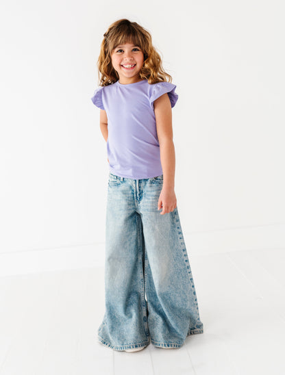 Young girl wearing a purple bamboo/cotton shirt and wide-leg jeans on a white background