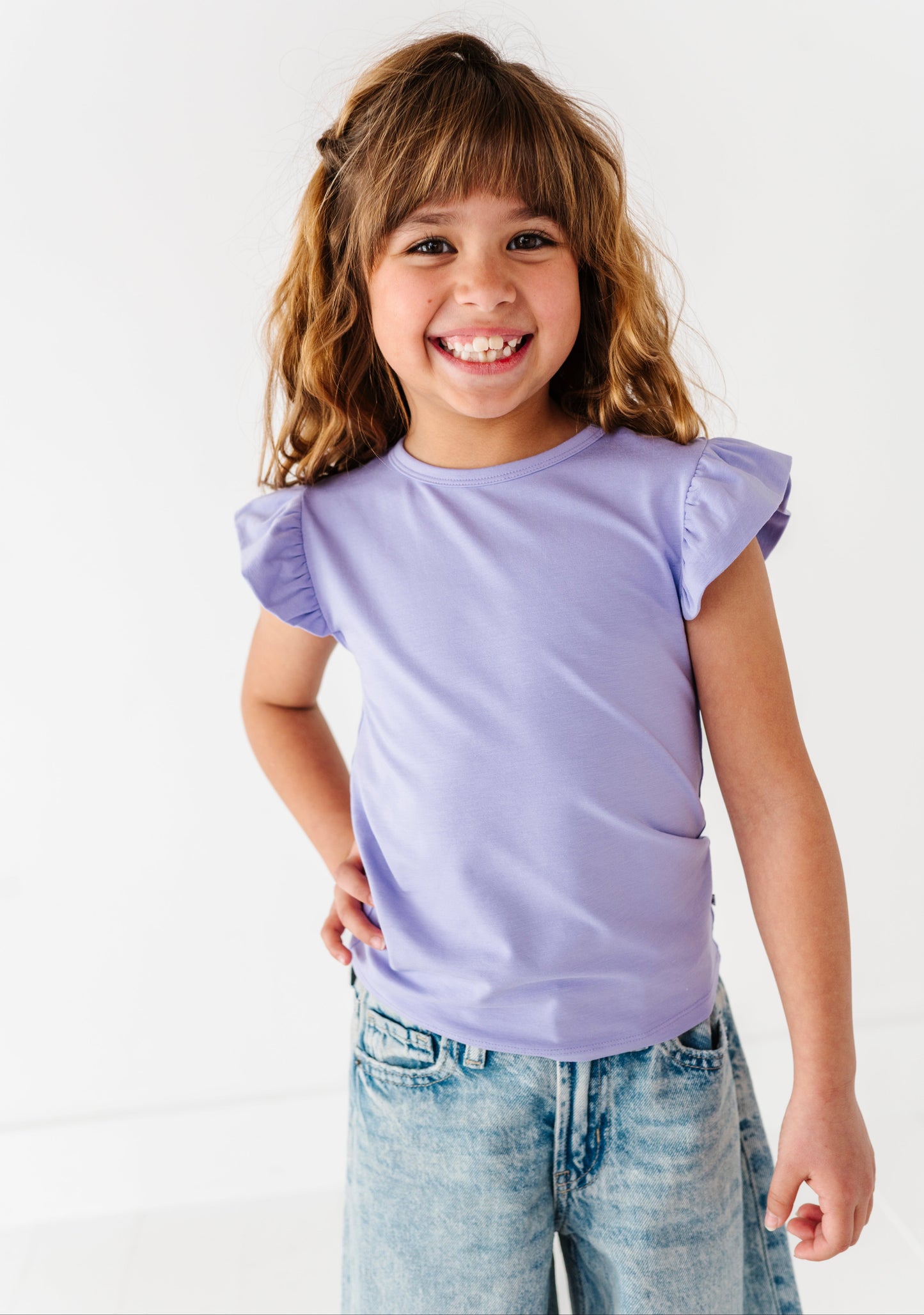 Young girl wearing a purple bamboo/cotton shirt and jeans on a white background