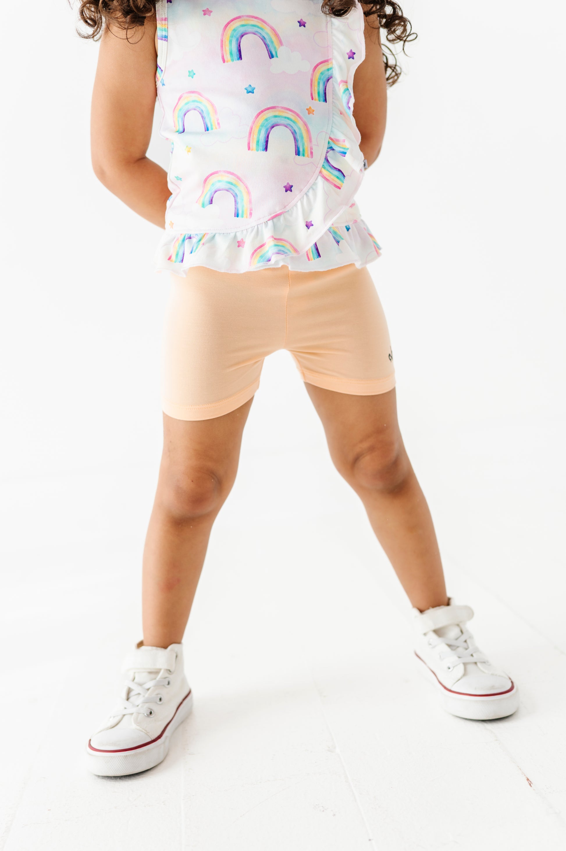 Child wearing a bamboo cotton watercolor rainbow-patterned peplum top and peach bamboo biker shorts on a white background