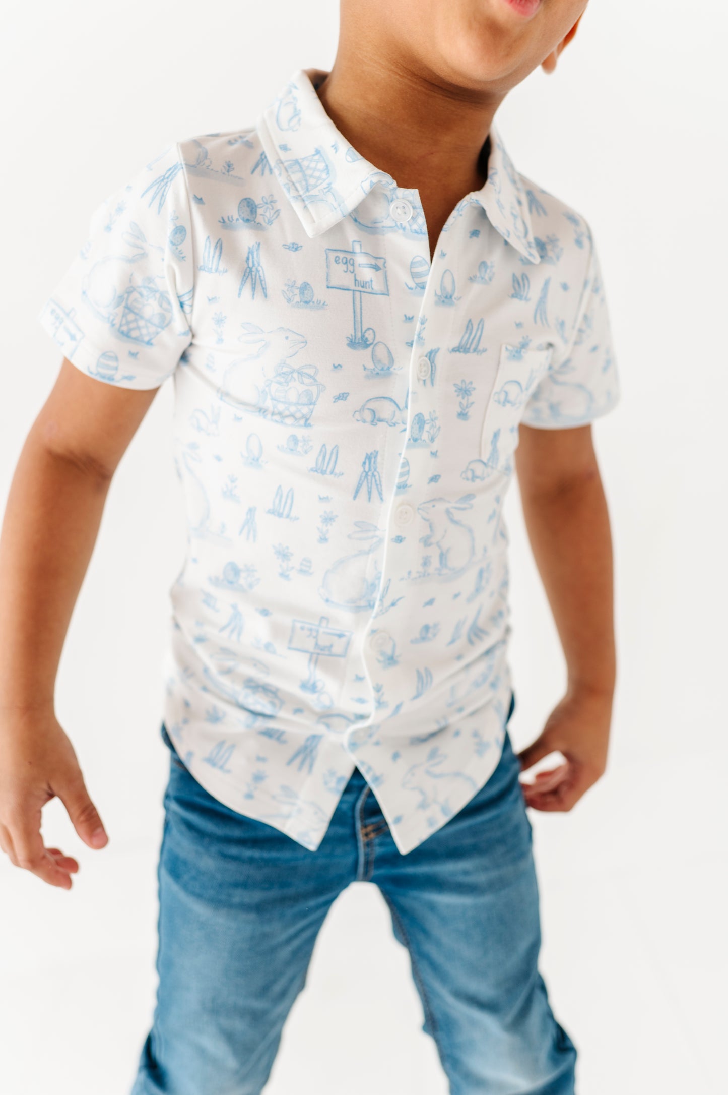 Child wearing a white shirt with blue patterns and blue jeans on a white background