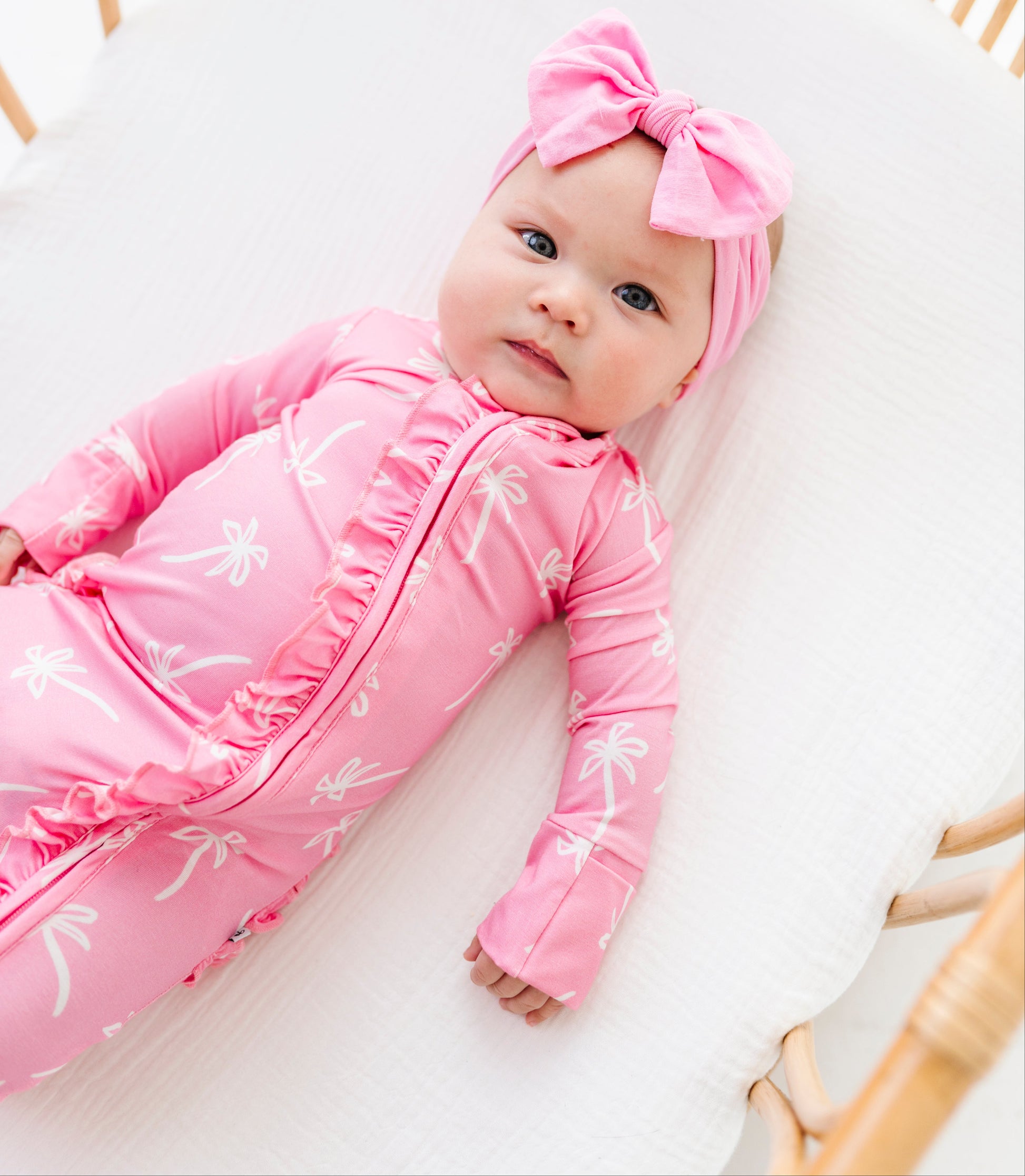 Baby in a pink outfit with a bow headband lying in a crib.