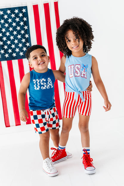 Two children wearing matching American-themed bamboo outfits in front of an American flag.