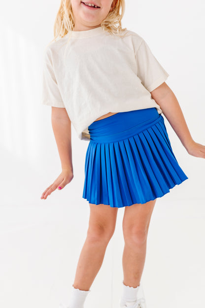 Child wearing a white shirt and blue pleated activewear skort on a white background