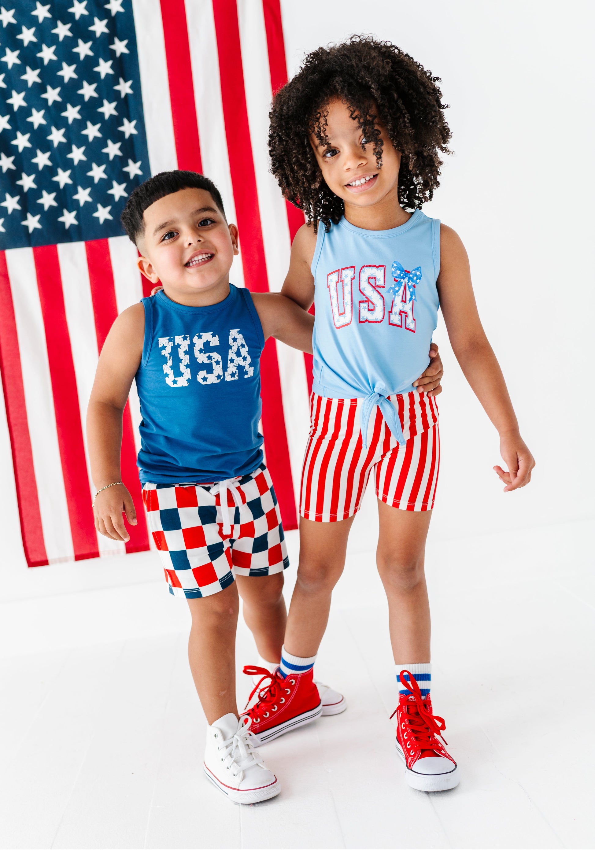 Two children wearing matching American-themed bamboo outfits in front of an American flag.
