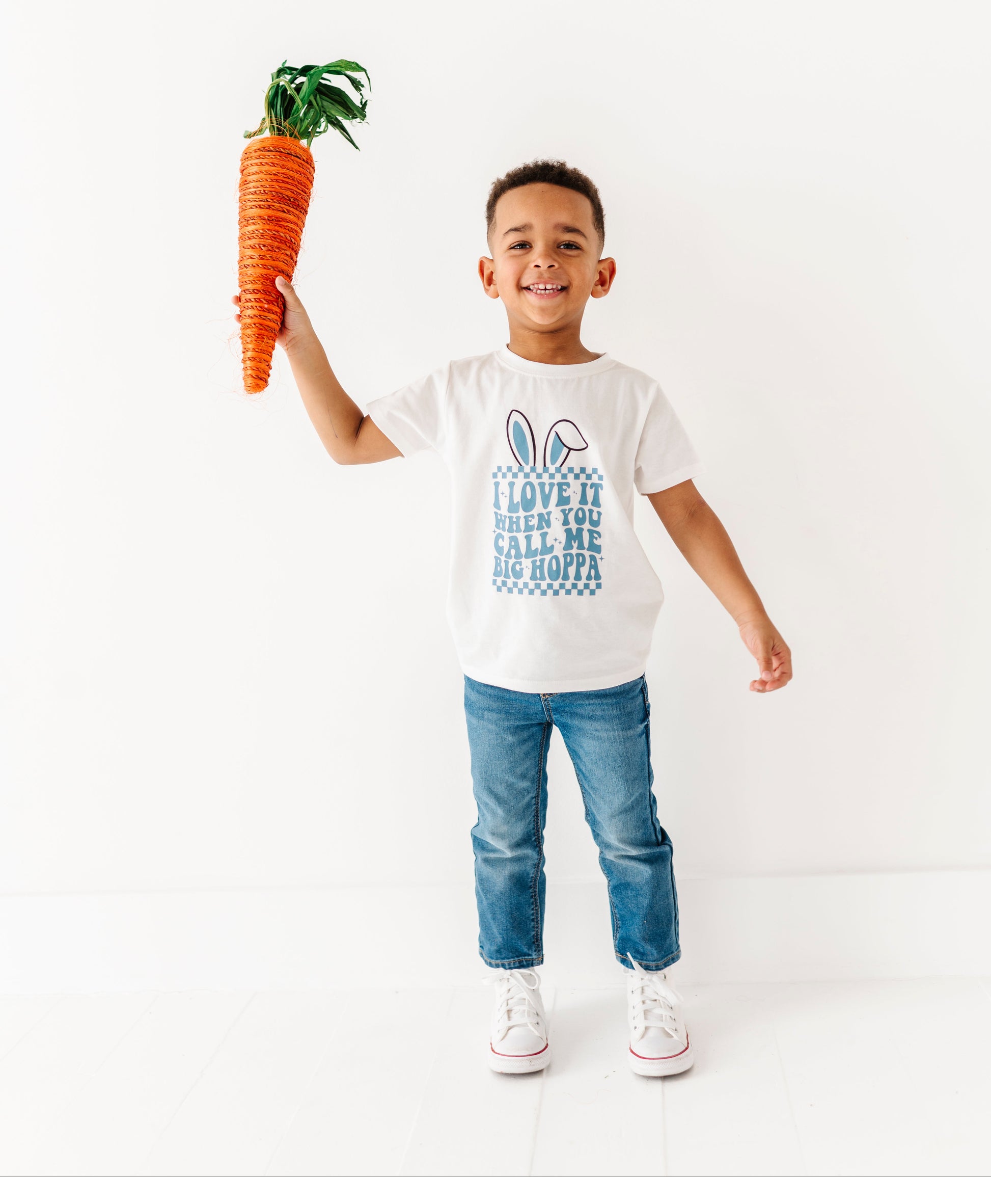 Child holding a toy carrot and wearing a white t-shirt with text on a white background