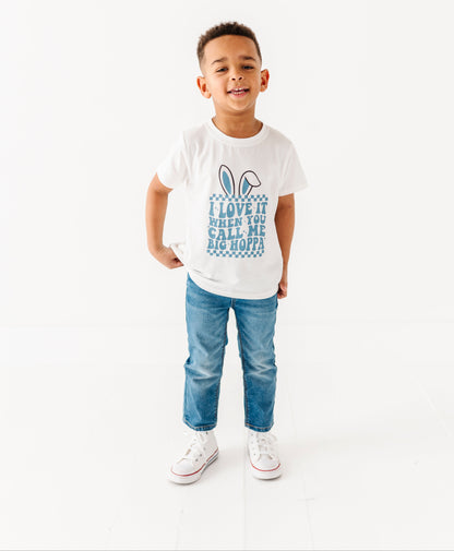 Child wearing a white t-shirt with text and graphics, standing against a white background
