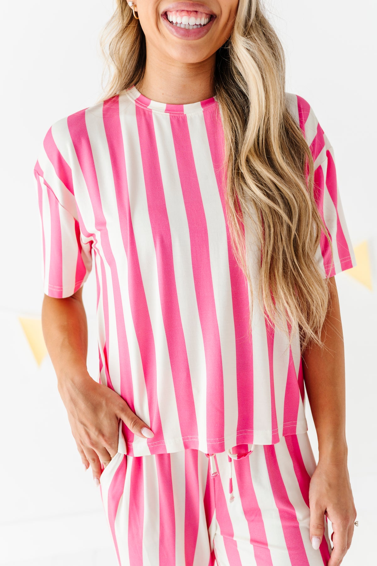 A woman wearing a pink and white vertically striped short-sleeve top and matching striped pants, shown from the mouth down against a clean white background.
