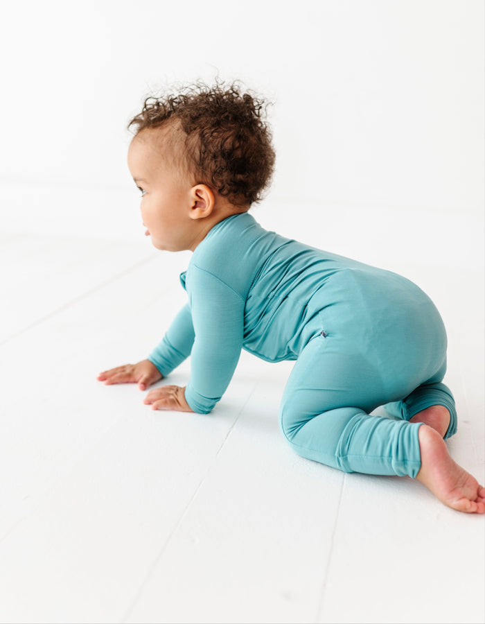 Baby in a slate blue convertible romper crawling on a white surface