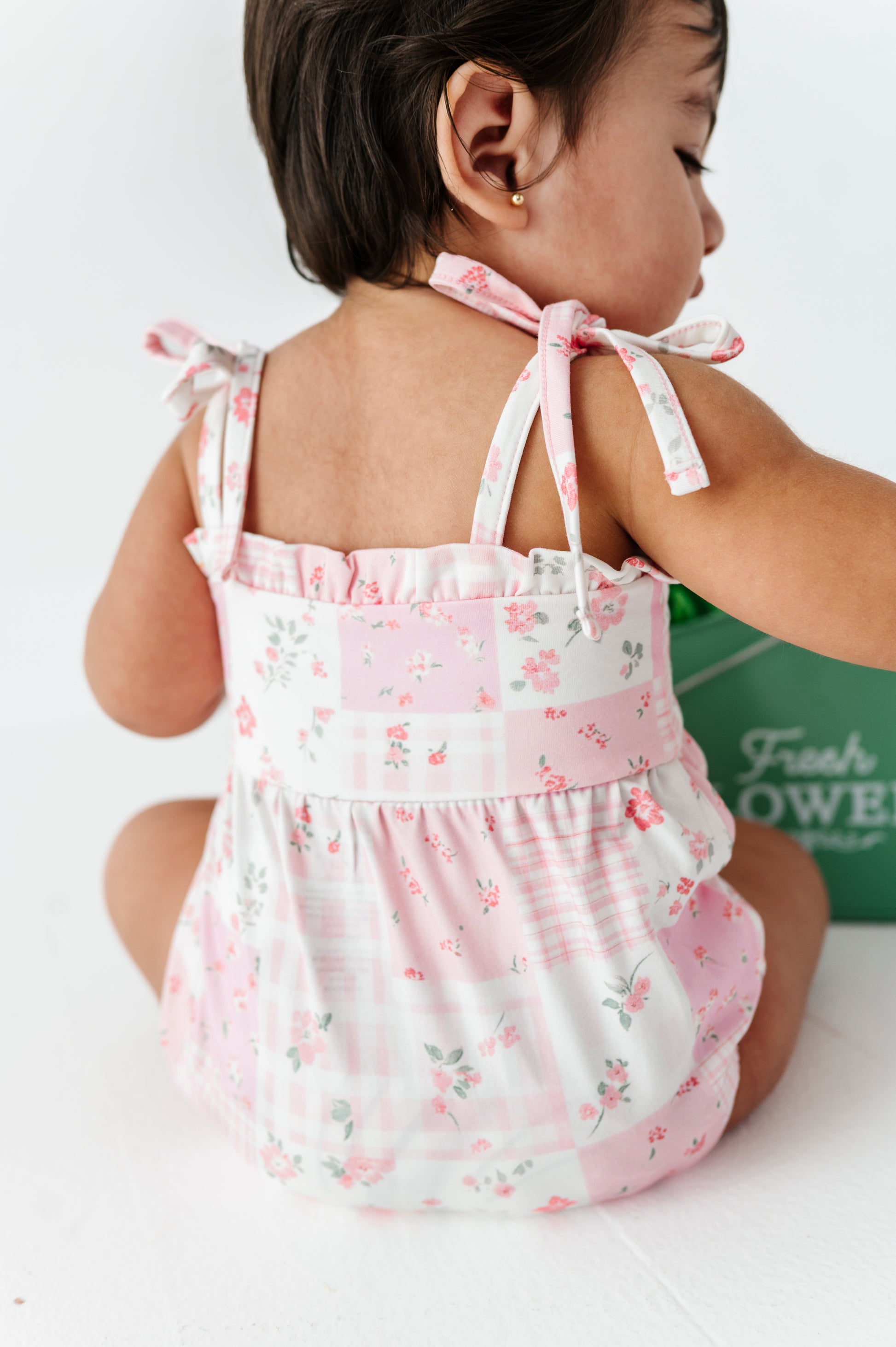 Child wearing a pink floral bamboo bubble romper sitting on a white surface.