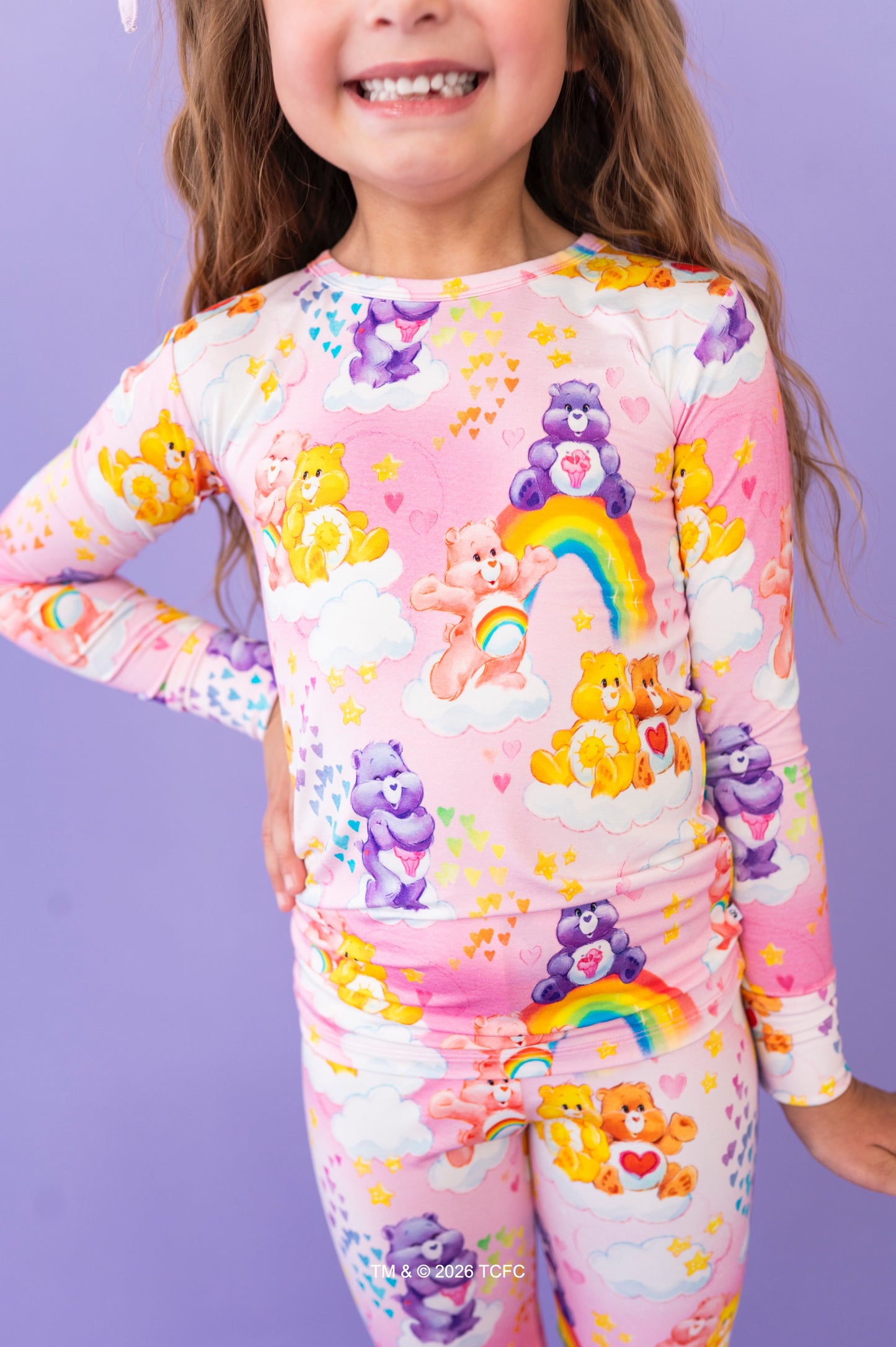 Child wearing a colorful Care Bears onesie against a purple background