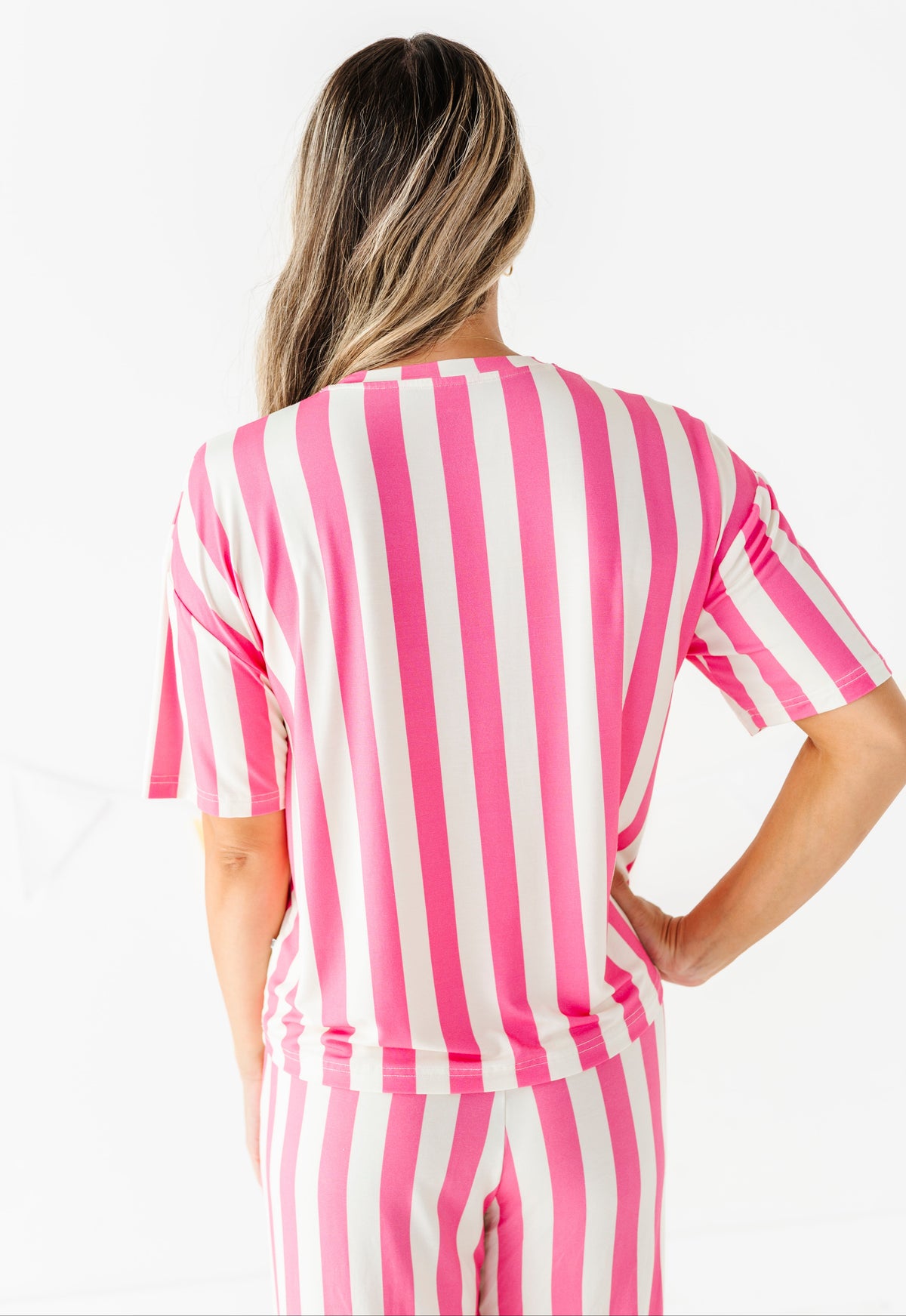 A woman shown from behind wearing a pink and white vertically striped short-sleeve top and matching striped pants against a plain white studio background.