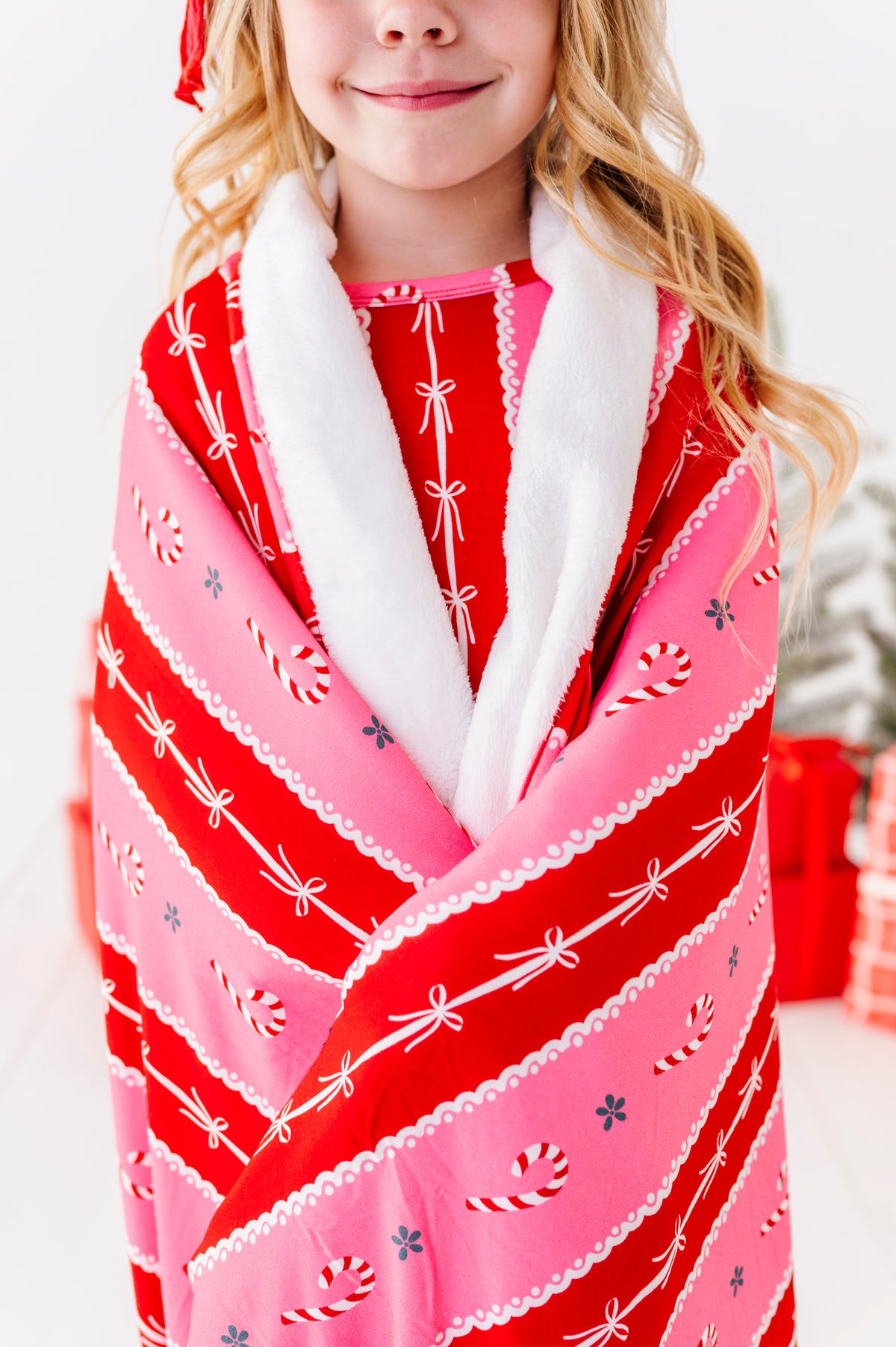 A little girl wrapped in a red-and-pink candy cane stripe bamboo blanket. It's a large, 50" x 55" plush blanket with super cozy backing and very soft bamboo front 