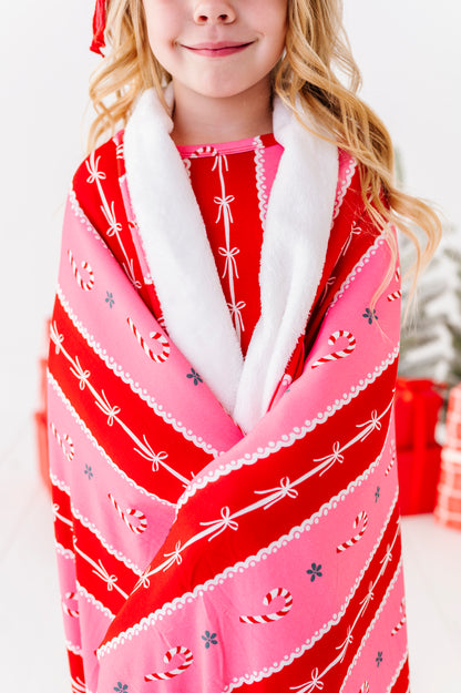 A little girl wrapped in a red-and-pink candy cane stripe bamboo blanket. It's a large, 50" x 55" plush blanket with super cozy backing and very soft bamboo front 