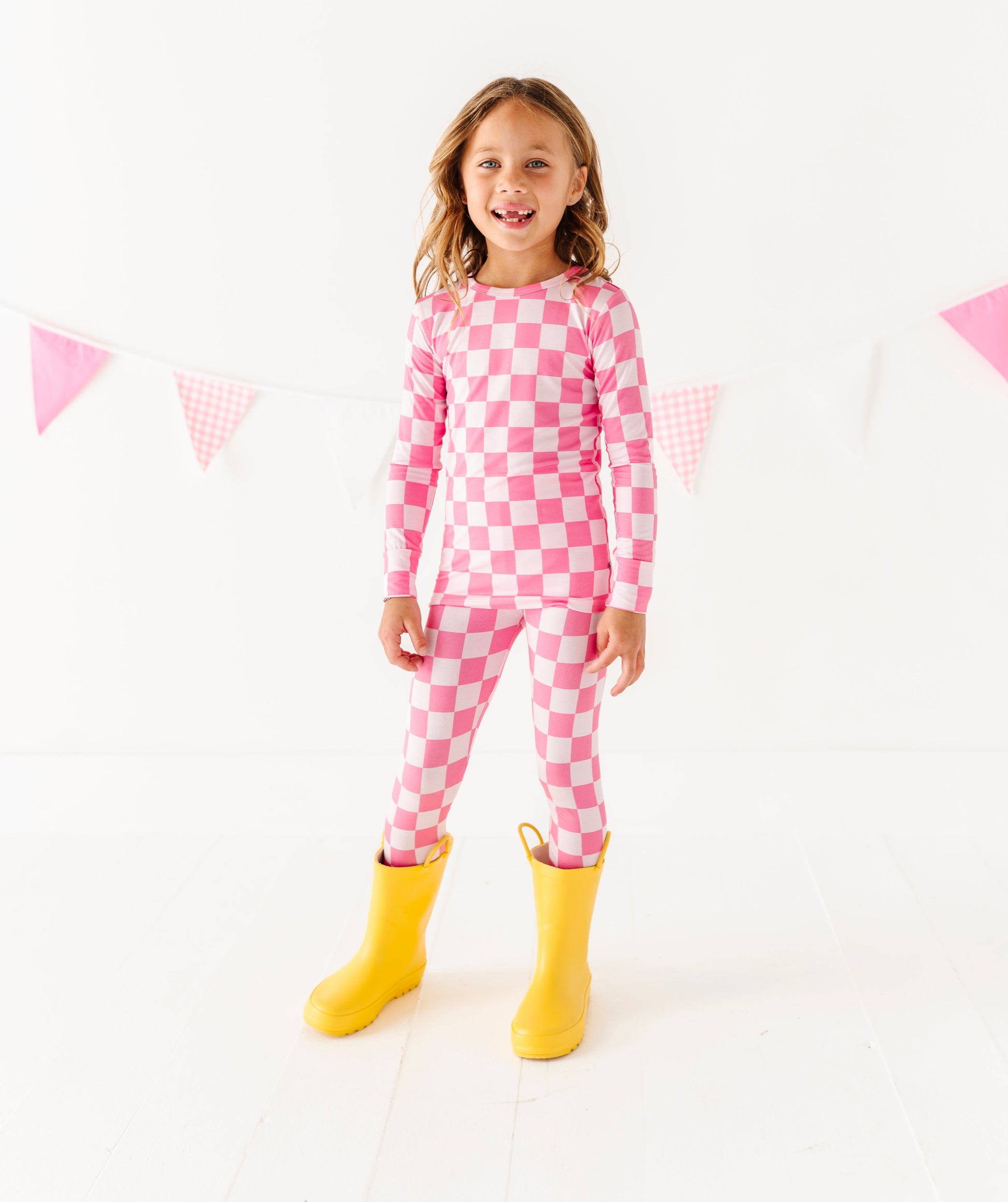 Child wearing pink checkered outfit with yellow boots on a white background