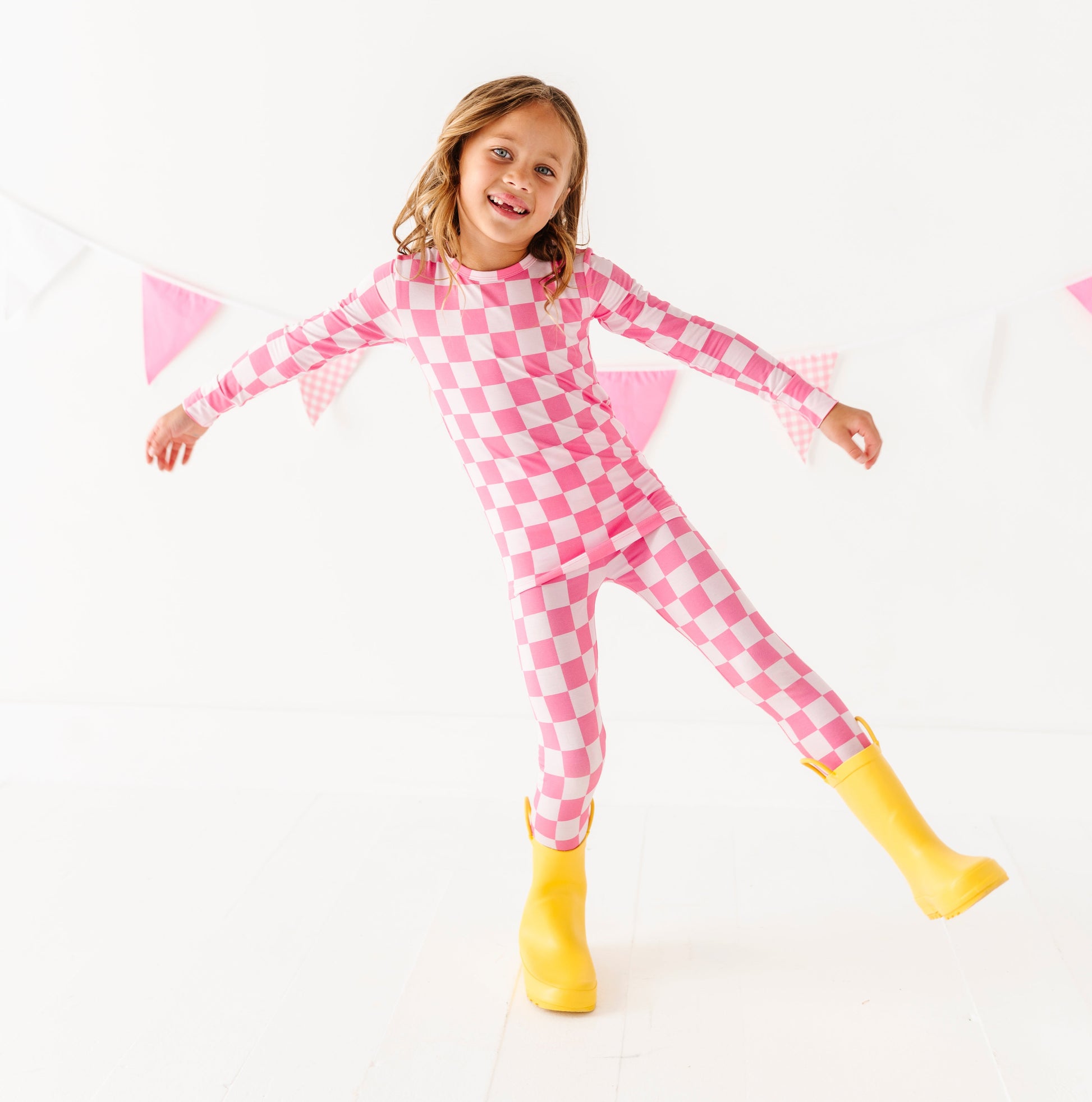 Child wearing pink checkered bamboo pajamas with yellow boots on a white background