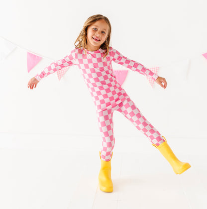 Child wearing pink checkered bamboo pajamas with yellow boots on a white background
